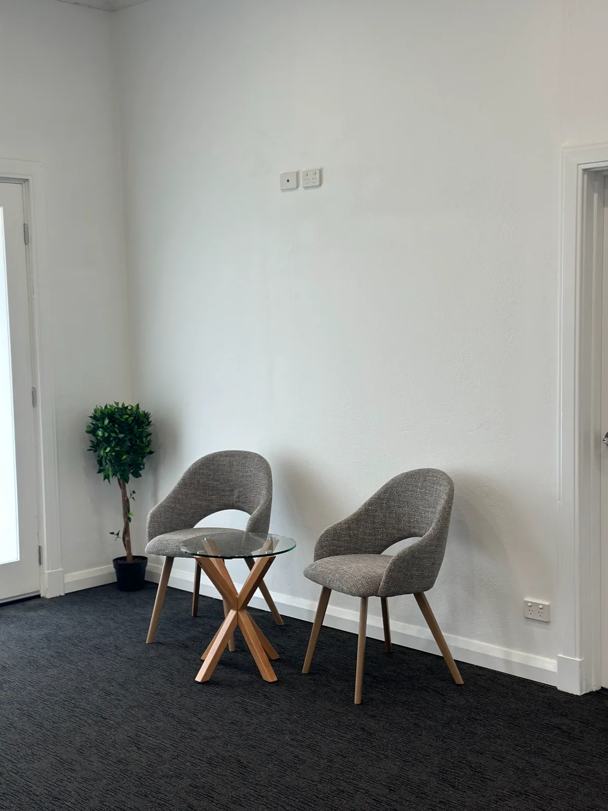 Two upholstered chairs either side of a small round table in a quiet consulting room at Adelaide Health Group