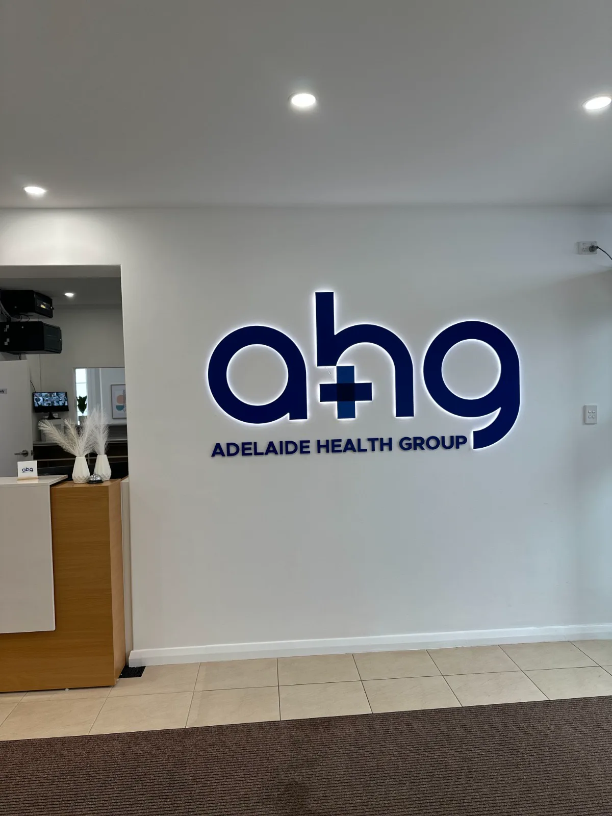 The illuminated Adelaide Health Group sign on the foyer wall beside the reception desk