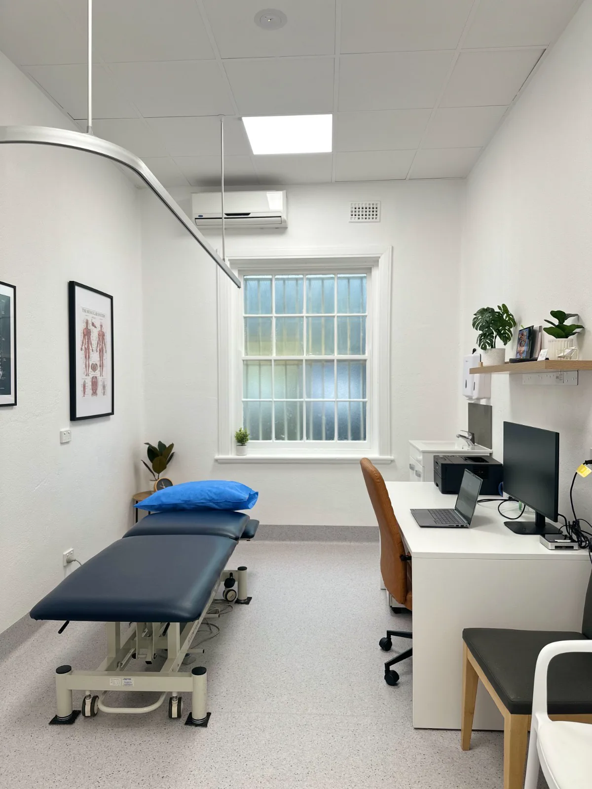 A treatment room at Adelaide Health Group with a plinth, a clinician desk and anatomical charts on the wall