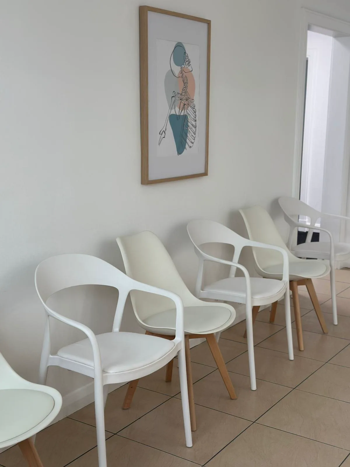 White chairs along the waiting room wall at Adelaide Health Group, beneath a framed anatomical print, with the corridor beyond
